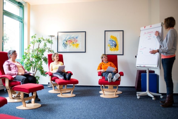 Drei Frauen sitzen, eine Frau erklärt an einem Whiteboard Drei Frauen sitzen, eine Frau erklärt an einem Whiteboard